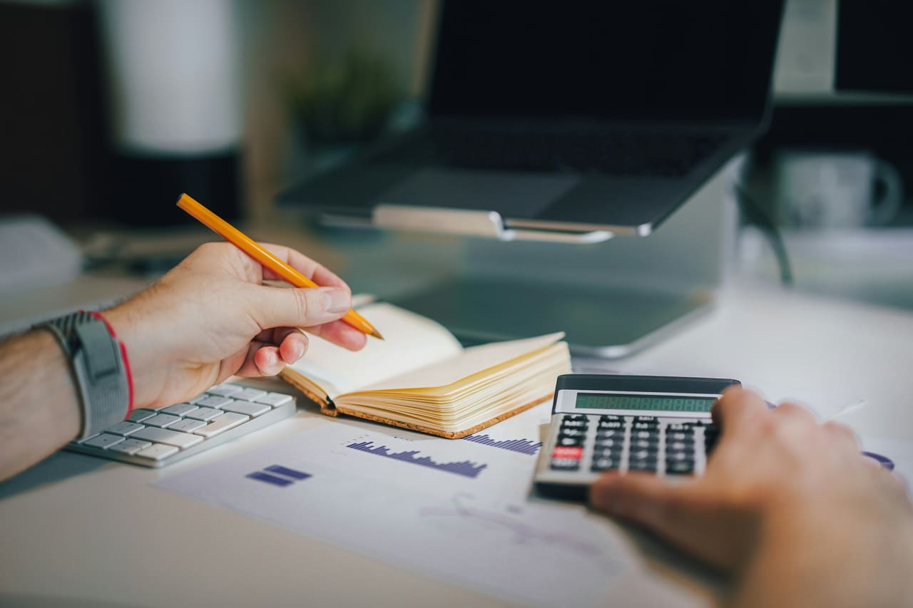 A person working through figures with a calculator, pencil and notebook