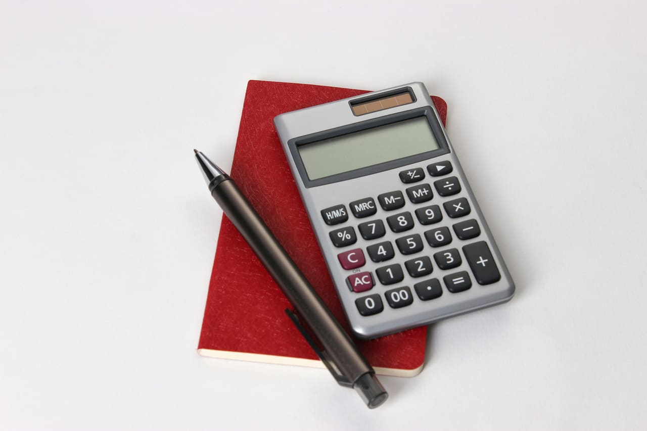 A silver calculator and a pen on a red notebook